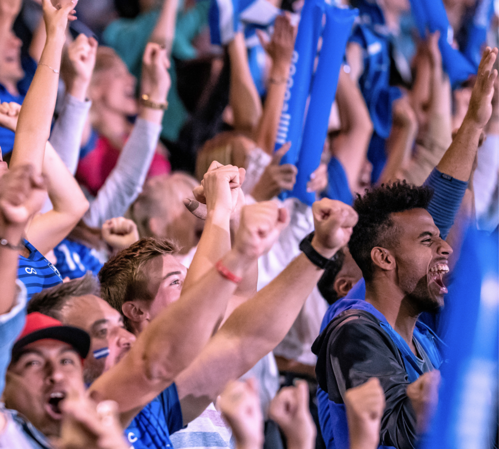 A group of sports fans raise their hands and cheer in unison